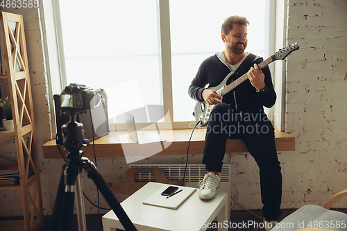 Image of Caucasian musician playing guitar during online concert at home isolated and quarantined, cheerful improvising