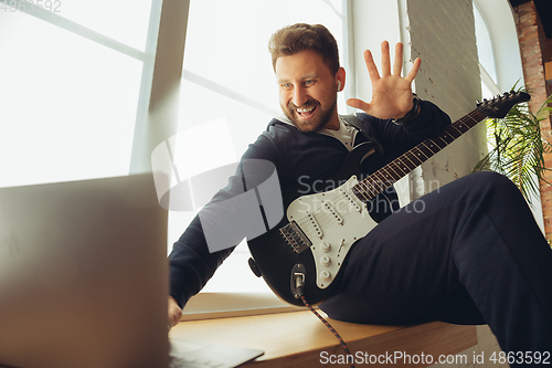 Image of Caucasian musician playing guitar during concert at home isolated and quarantined, cheerful improvising with the band connected online