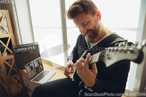 Image of Caucasian musician playing guitar during concert at home isolated and quarantined, cheerful improvising with the band connected online