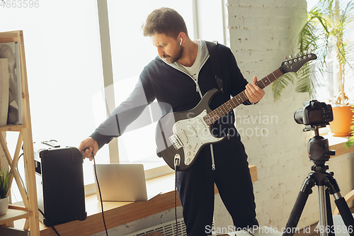 Image of Caucasian musician playing guitar during online concert at home isolated and quarantined, tuning the stream