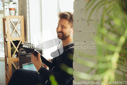 Image of Caucasian musician playing guitar during online concert at home isolated and quarantined, cheerful improvising