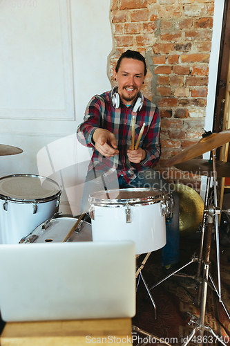 Image of Caucasian musician playing drumms during online concert with the band at home isolated and quarantined, greeting audience