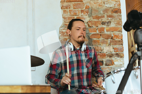 Image of Caucasian musician playing drumms during online concert with the band at home isolated and quarantined, inspired improvising