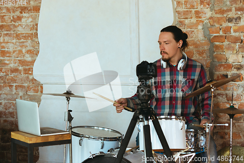 Image of Caucasian musician playing drumms during online concert with the band at home isolated and quarantined, inspired improvising