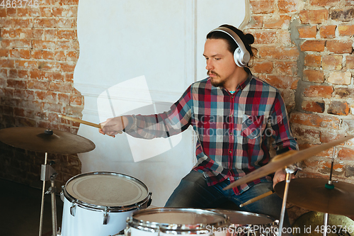 Image of Caucasian musician playing drumms during online concert with the band at home isolated and quarantined, inspired improvising