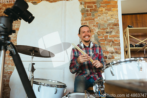 Image of Caucasian musician playing drumms during online concert with the band at home isolated and quarantined, greeting audience