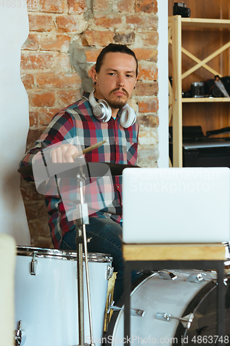 Image of Caucasian musician playing drumms during online concert with the band at home isolated and quarantined, inspired improvising