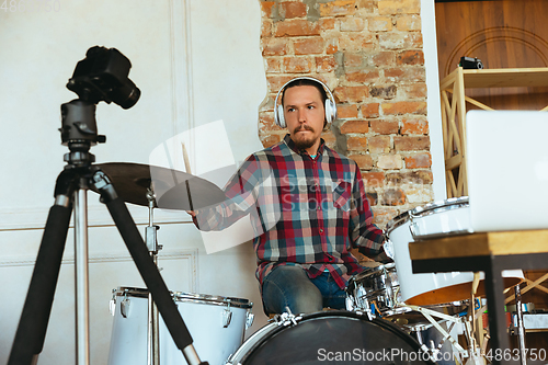 Image of Caucasian musician playing drumms during online concert with the band at home isolated and quarantined, inspired improvising