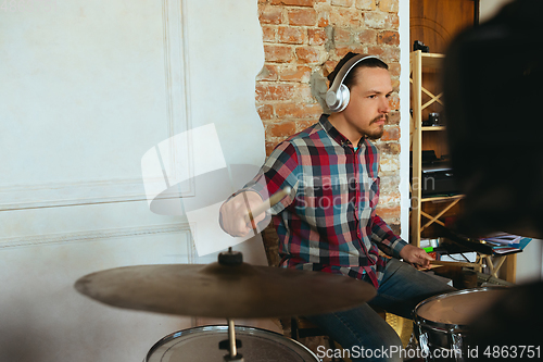 Image of Caucasian musician playing drumms during online concert with the band at home isolated and quarantined, inspired improvising