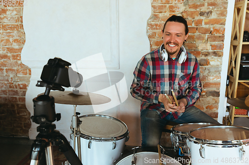 Image of Caucasian musician playing drumms during online concert with the band at home isolated and quarantined, smiling, cheerful