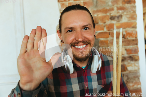 Image of Caucasian musician greeting audience during concert at home isolated and quarantined, smiling, cheerful