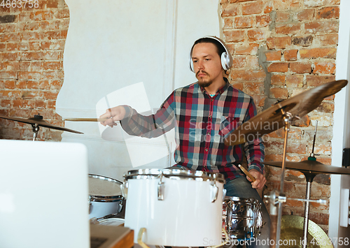 Image of Caucasian musician playing drumms during online concert with the band at home isolated and quarantined, inspired improvising