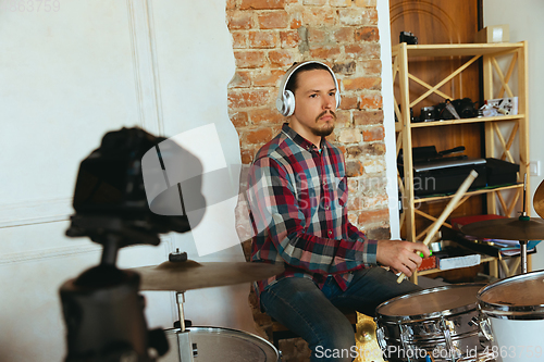 Image of Caucasian musician playing drumms during online concert with the band at home isolated and quarantined, inspired improvising