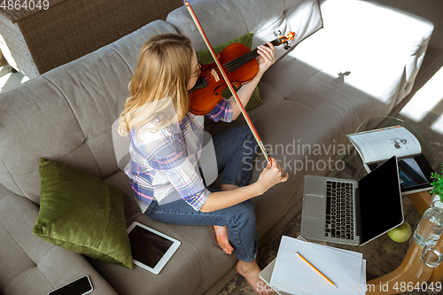 Image of Young woman studying at home during online courses or free information by herself, playing violin, improvising