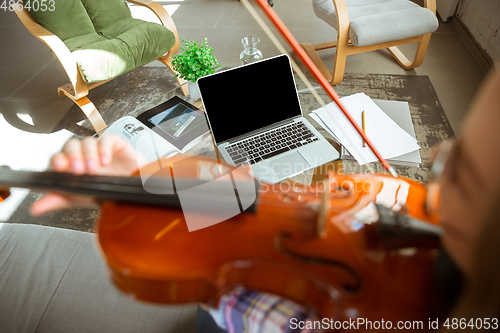 Image of Young woman studying at home during online courses or free information by herself, playing violin, improvising