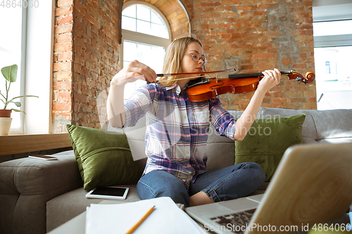 Image of Young woman studying at home during online courses or free information by herself, playing violin, improvising