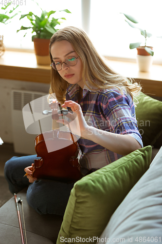 Image of Young woman studying at home during online courses or free information by herself, playing violin, improvising