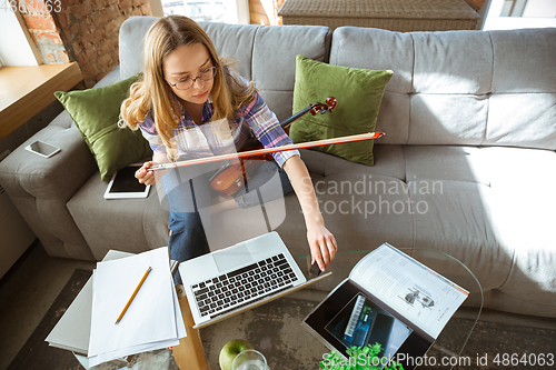 Image of Young woman studying at home during online courses or free information by herself, playing violin, improvising