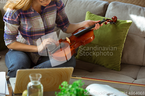 Image of Young woman studying at home during online courses or free information by herself, playing violin, improvising