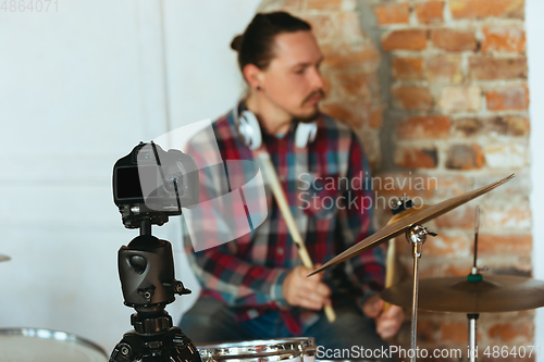 Image of Caucasian musician playing drumms during online concert with the band at home isolated and quarantined, inspired improvising