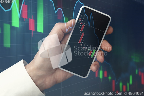 Image of Hands holding smartphone showing graphs going down. Double exposure with graphs, digital. Virus alert, coronavirus pandemic, crisis, unemployment