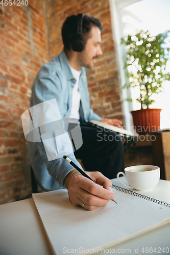 Image of Caucasian musician playing hand drum during online concert at home isolated and quarantined, making notes, focus on hand