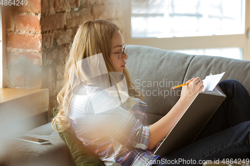 Image of Young woman studying at home during online courses or free information by herself, making notes