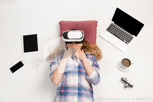 Image of Emotional caucasian woman using VR-headsed, surrounded by gadgets isolated on white studio background, technologies. Shocked, scared