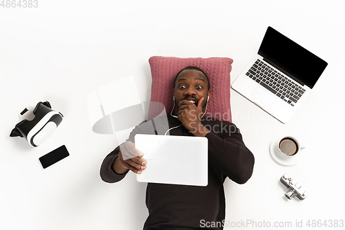 Image of Emotional african-american man using tablet surrounded by gadgets isolated on white studio background, technologies connecting people. Shocked, scared