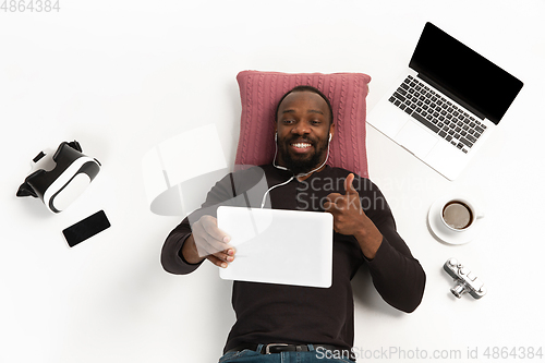 Image of Emotional african-american man using tablet surrounded by gadgets isolated on white studio background, technologies connecting people. Smiling, thumb up