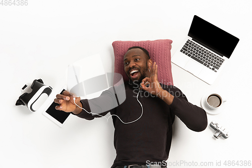 Image of Emotional african-american man using phone surrounded by gadgets isolated on white studio background, technologies connecting people. Online meeting, selfie