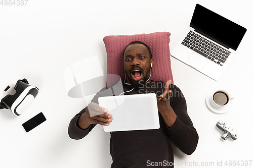 Image of Emotional african-american man using tablet surrounded by gadgets isolated on white studio background, technologies. Angry asking