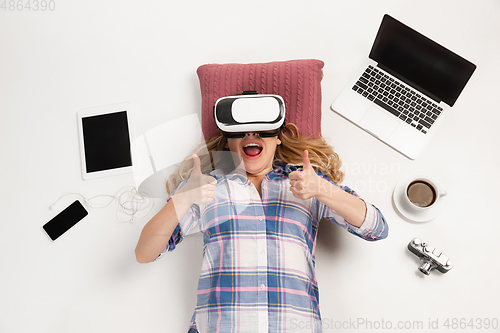 Image of Emotional caucasian woman using VR-headsed, surrounded by gadgets isolated on white studio background, technologies. Happy shows thumbs up