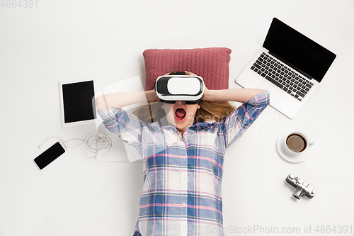 Image of Emotional caucasian woman using VR-headsed, surrounded by gadgets isolated on white studio background, technologies. Shocked, scared