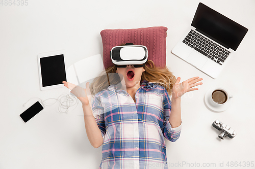 Image of Emotional caucasian woman using VR-headsed, surrounded by gadgets isolated on white studio background, technologies. Shocked