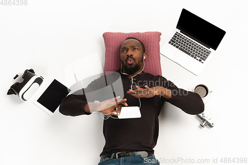 Image of Emotional african-american man using phone surrounded by gadgets isolated on white studio background, technologies connecting people. Inspired singing