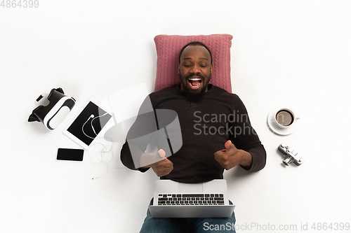 Image of Emotional african-american man using laptop surrounded by gadgets isolated on white studio background, technologies. Showing thumbs up