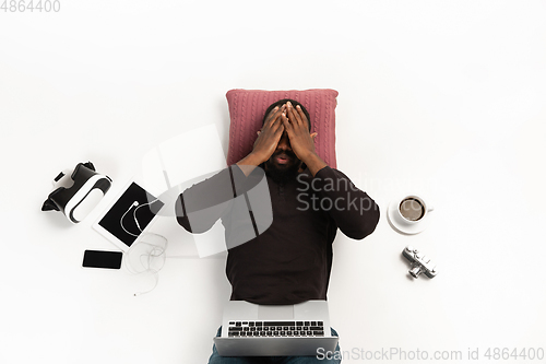 Image of Emotional african-american man using laptop surrounded by gadgets isolated on white studio background, technologies. Shocked