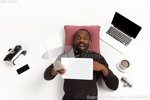 Image of Emotional african-american man using tablet surrounded by gadgets isolated on white studio background, technologies connecting people. Shocked, scared