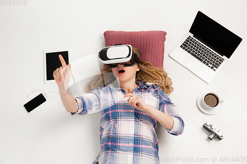 Image of Emotional caucasian woman using VR-headsed, surrounded by gadgets isolated on white studio background, technologies. Touching