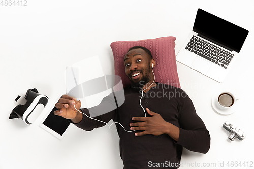 Image of Emotional african-american man using phone surrounded by gadgets isolated on white studio background, technologies connecting people. Online meeting, selfie