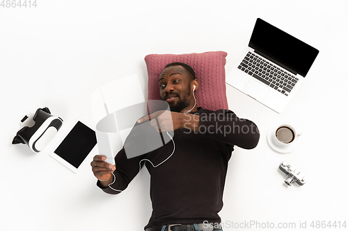 Image of Emotional african-american man using phone surrounded by gadgets isolated on white studio background, technologies connecting people. Selfie