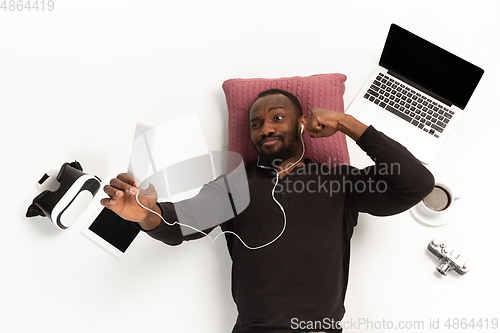 Image of Emotional african-american man using phone surrounded by gadgets isolated on white studio background, technologies connecting people. Online meeting, selfie