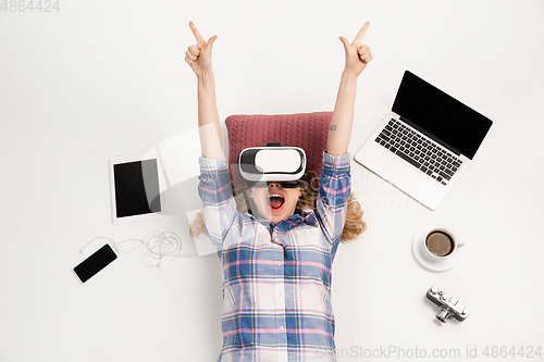 Image of Emotional caucasian woman using VR-headsed, surrounded by gadgets isolated on white studio background, technologies. Happy winning