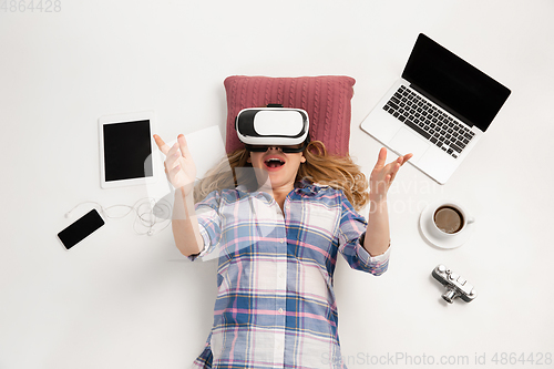 Image of Emotional caucasian woman using VR-headsed, surrounded by gadgets isolated on white studio background, technologies. Happy, greeting