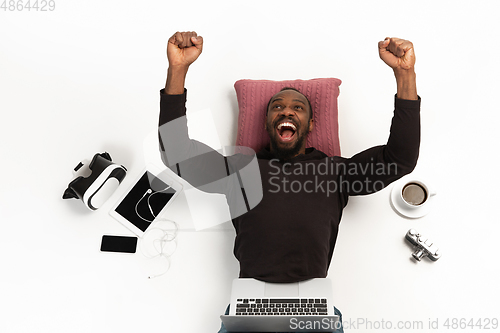 Image of Emotional african-american man using laptop surrounded by gadgets isolated on white studio background, technologies. Crazy winning