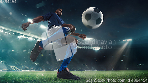 Image of Football or soccer player in action on stadium with flashlights, kicking ball for winning goal, wide angle. Action, competition in motion