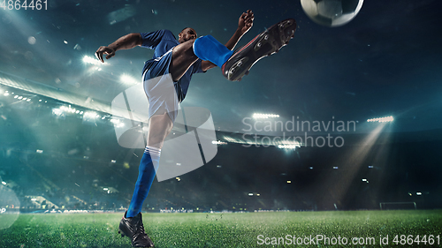 Image of Football or soccer player in action on stadium with flashlights, kicking ball for winning goal, wide angle. Action, competition in motion