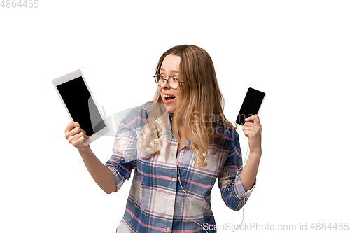 Image of Emotional caucasian woman using gadgets on white studio background, technologies. Crazy happy shows tablet and smartphone