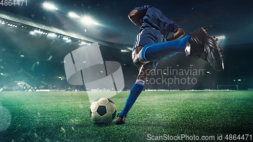 Image of Football or soccer player in action on stadium with flashlights, kicking ball for winning goal, wide angle. Action, competition in motion